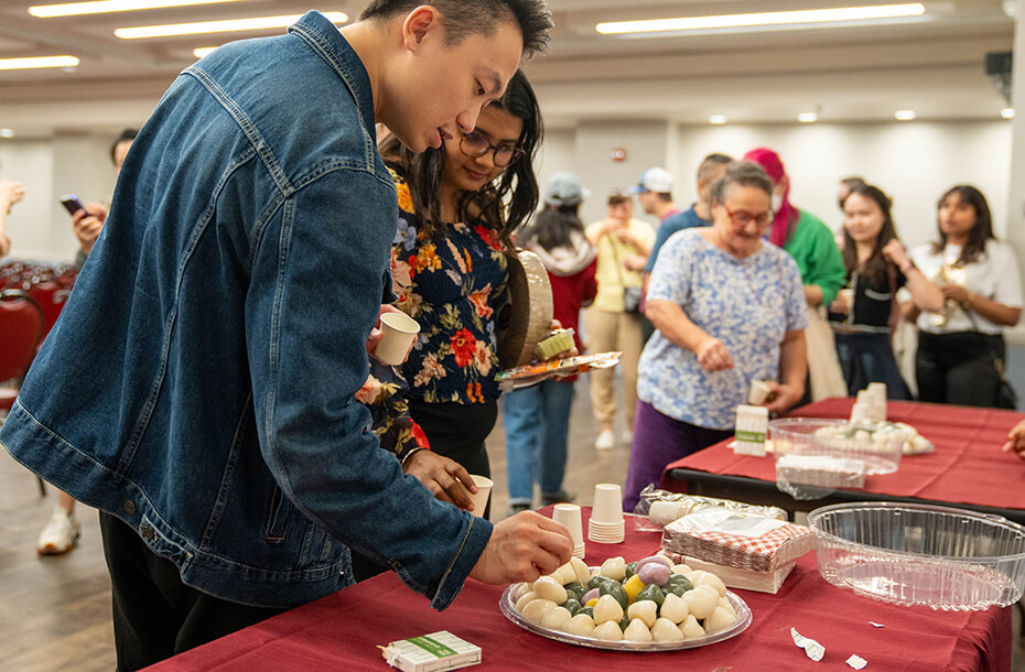 A man and woman use toothpicks to serve themselves. There is line behind them of people waiting for their turn to serve themselves food.