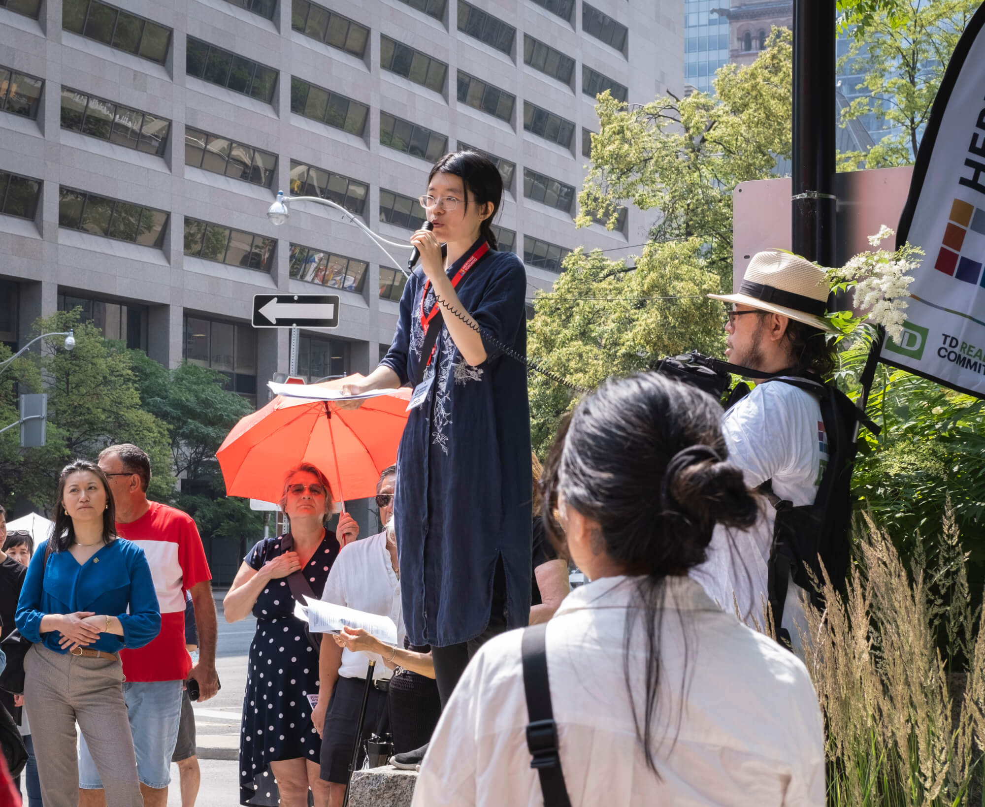 Image of a woman standing on a rock speaking to a group of people through a microphone.