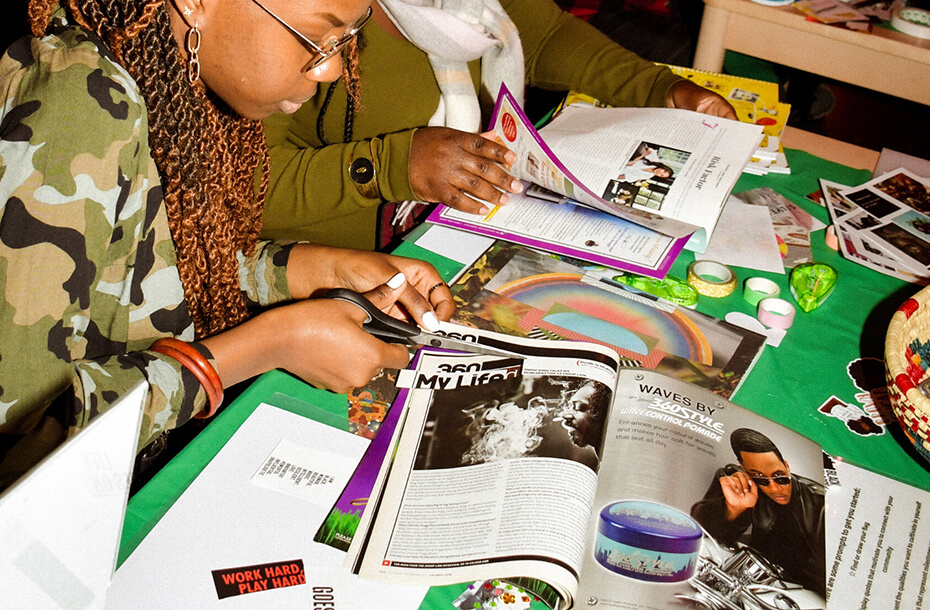 Image of magazines and craft supplies on a table being used to create vision boards. Two people are sitting at the table cutting magazines.