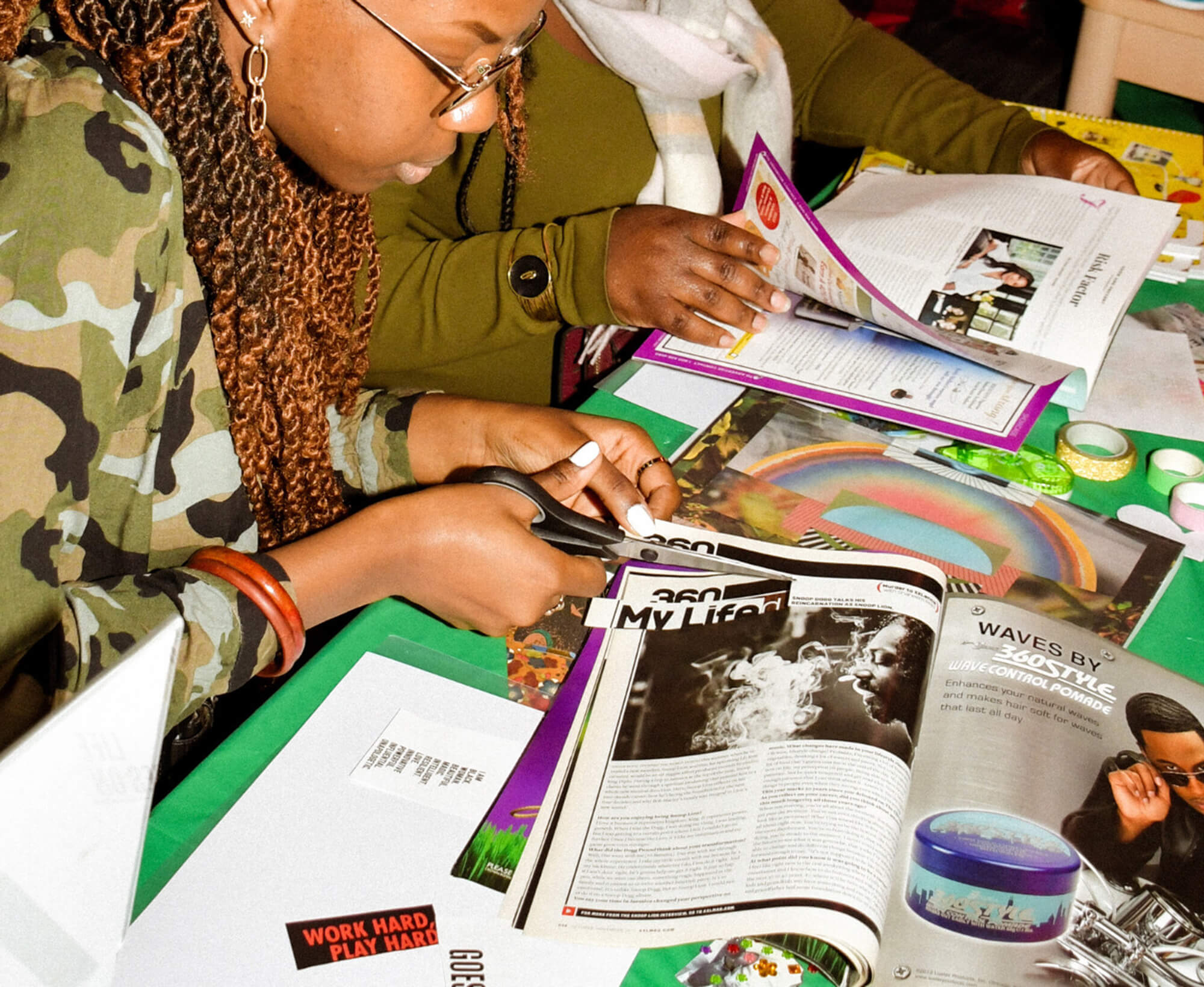 Image of magazines and craft supplies on a table being used to create vision boards. Two people are sitting at the table cutting magazines.