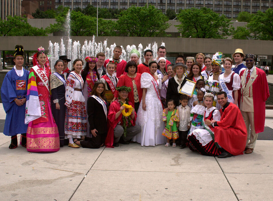 A large group of people, dressed in a variety of traditional costumes, pose for a photo following the conclusion of the 2002 Caravan festival pageant.