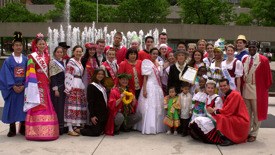 A large group of people, dressed in a variety of traditional costumes, pose for a photo following the conclusion of the 2002 Caravan festival pageant.
