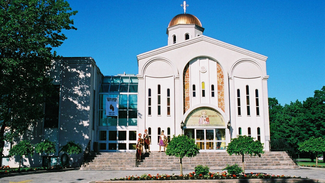 Four people in costume are posed to the left of a Macedonian Church acting as the Skopje Pavilion for the Metro International Caravan Festival of 2002. The people in this image are costumed in ancient Macedonian combat attire.