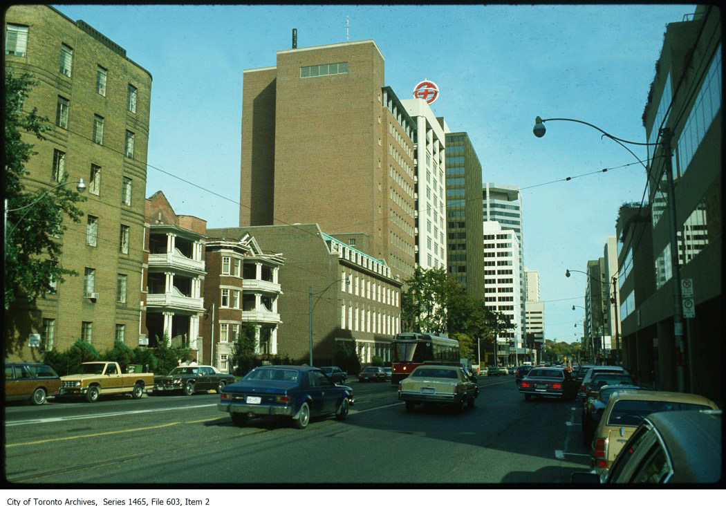 A colour image of a street scene. Amid low-rise and high-rise apartment and office towers, cars can be seen driving on the street.