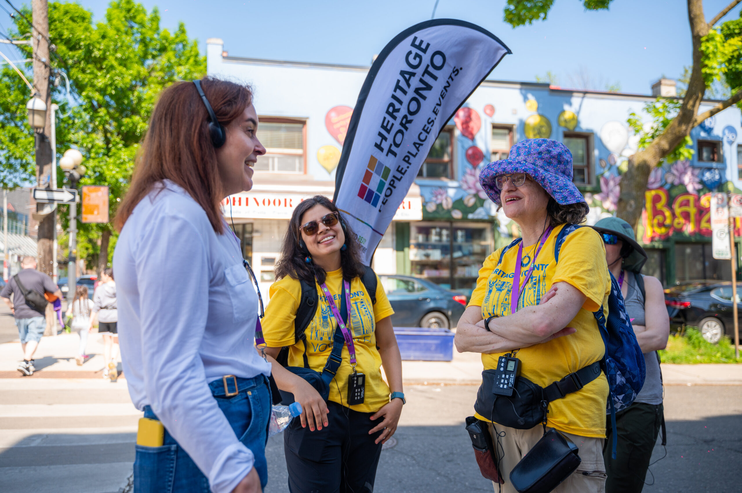 Three people standing with eachother and talking. Two appear to be volunteers as they are wearing volunteer t-shirts.