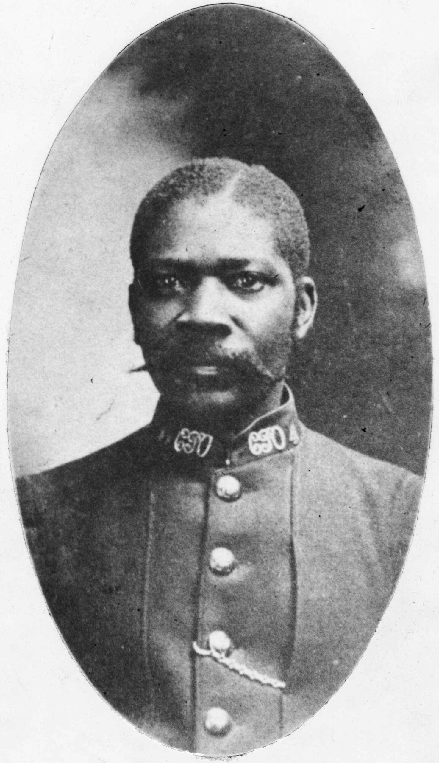 A black and white portrait style photograph of a black man with a moustache in a 19th century letter carrier uniform.