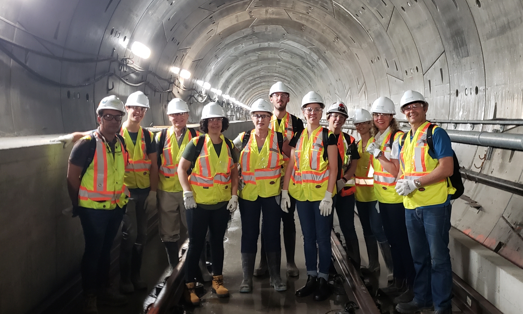 Group of people standing in a tunnel in hard hats and reflective vests.