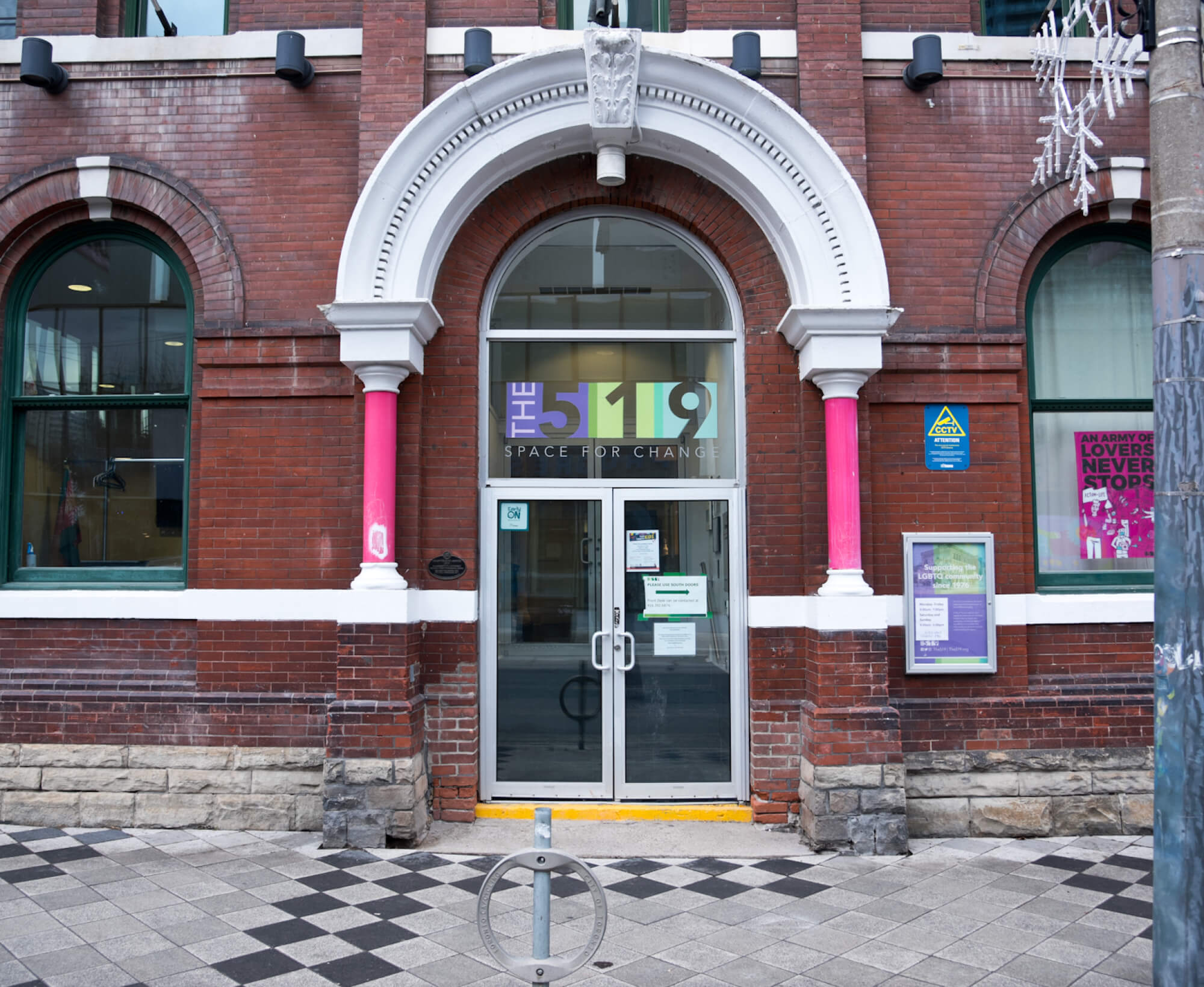 Image of the entryway of a red brick building with white accents. Above the doorway is a decorative white stone arch supported by pink vertical columns mounted on brick plinths.