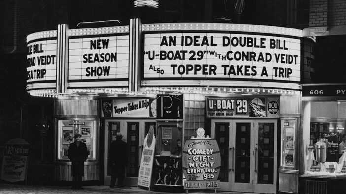 A theatre with a vertical sign spelling "Pylon". Billing on the marquee reads "An Ideal Double Bill 'U-Boat' with Conrad Veidt also Topper Takes a Trip".