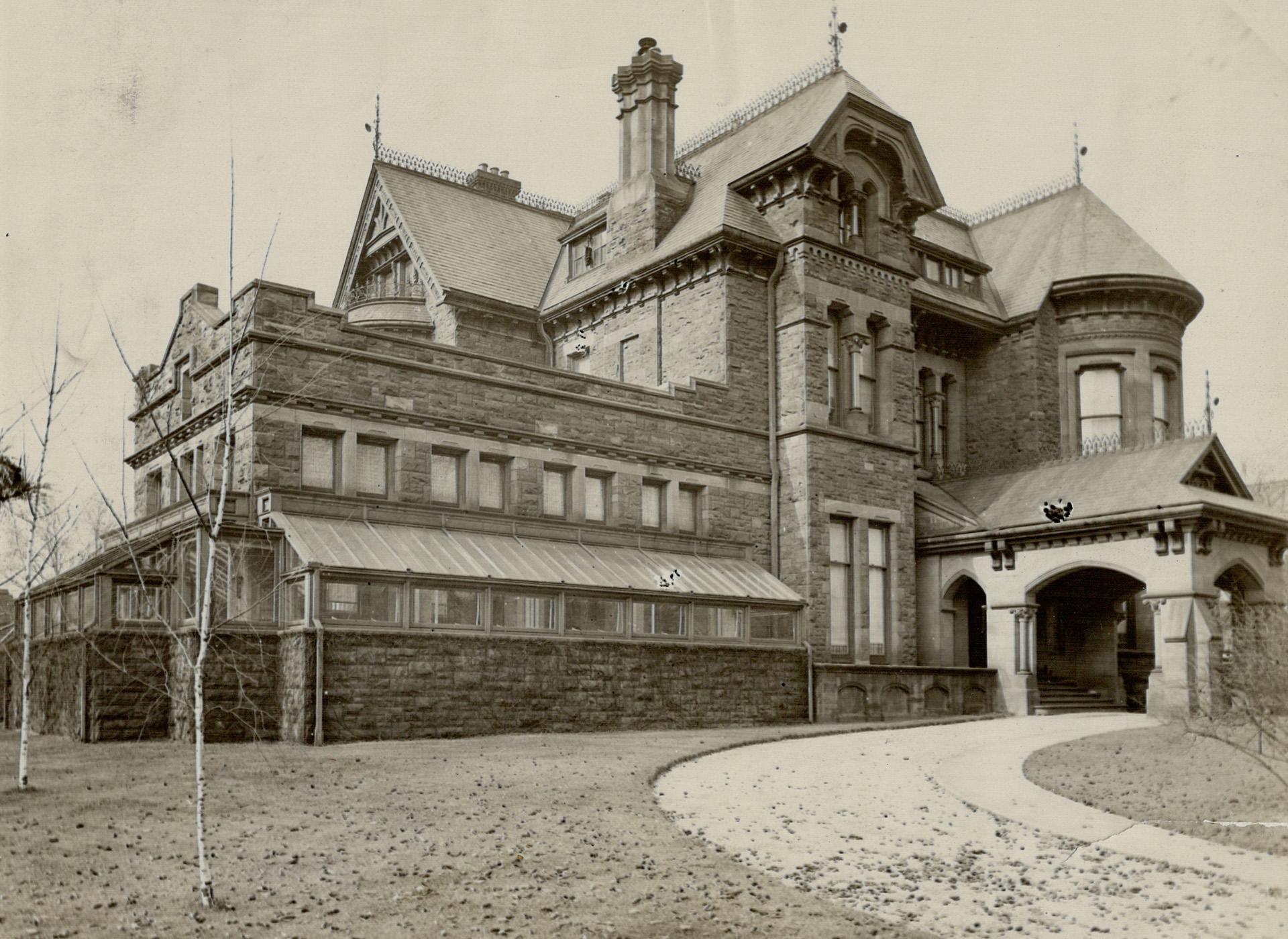 A large Victorian-style mansion is seen from the home’s driveway. Leaves lie on the home’s lawn.