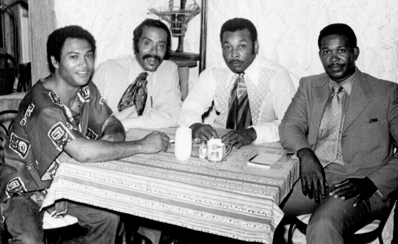 Image of four men seated at a small restaurant table posing for a photograph.