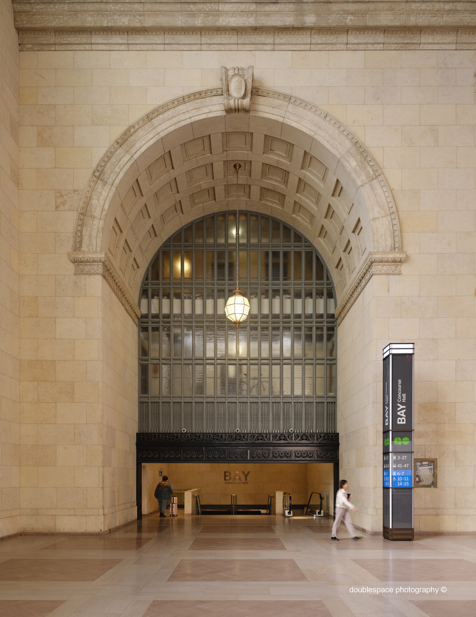 Large ornate archway in a beige stone wall. The back of the upper arch is caged with stairs descending under the archway.