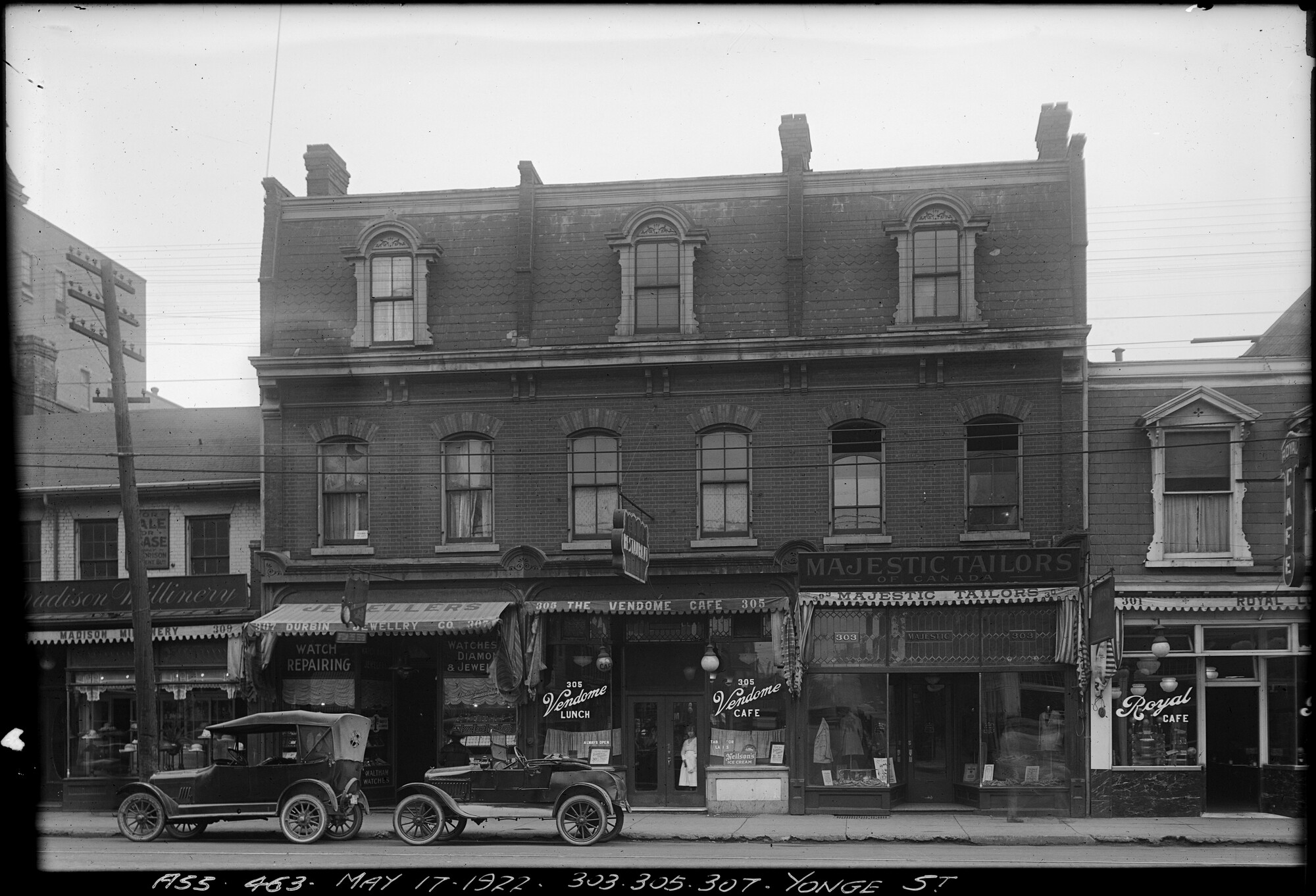 Black and white image of a row of stores on the ground floor of a three-storey building.