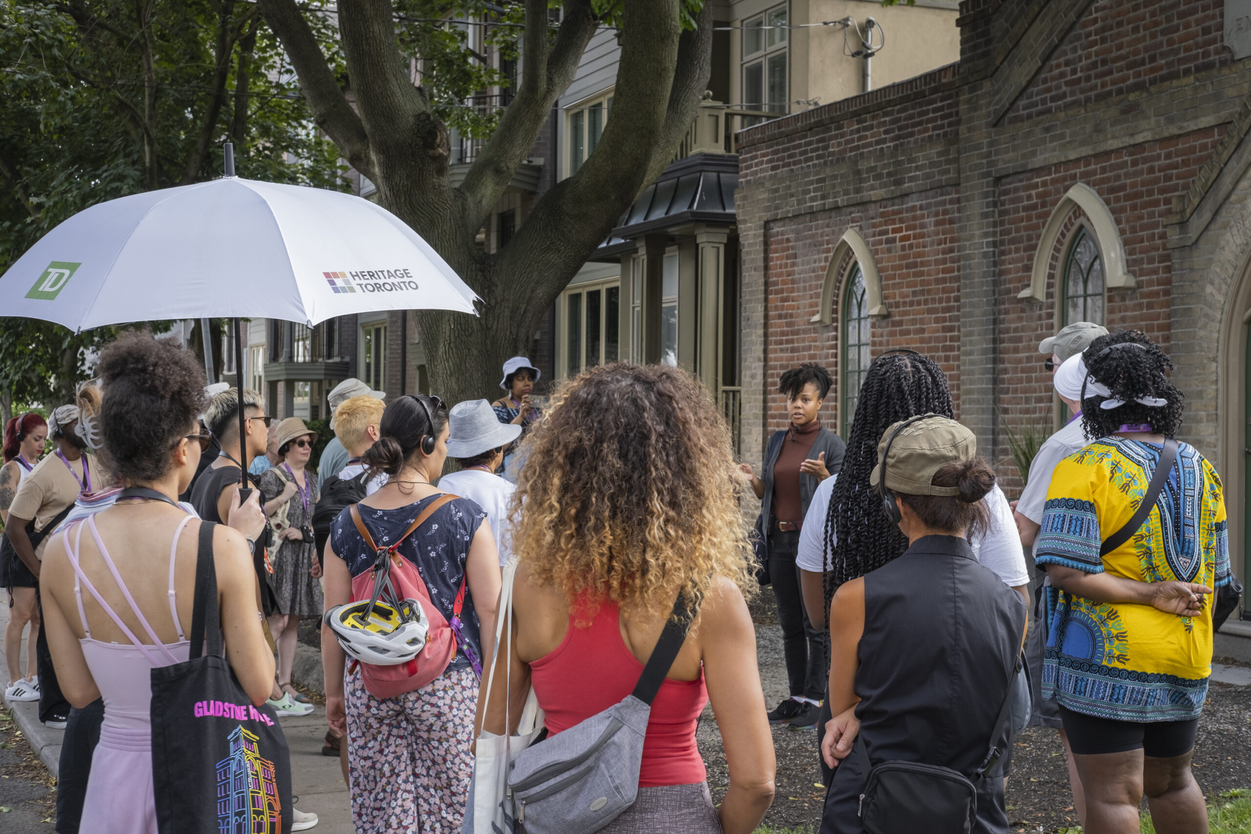 Group of people face away from the camera listening to a woman in the background.