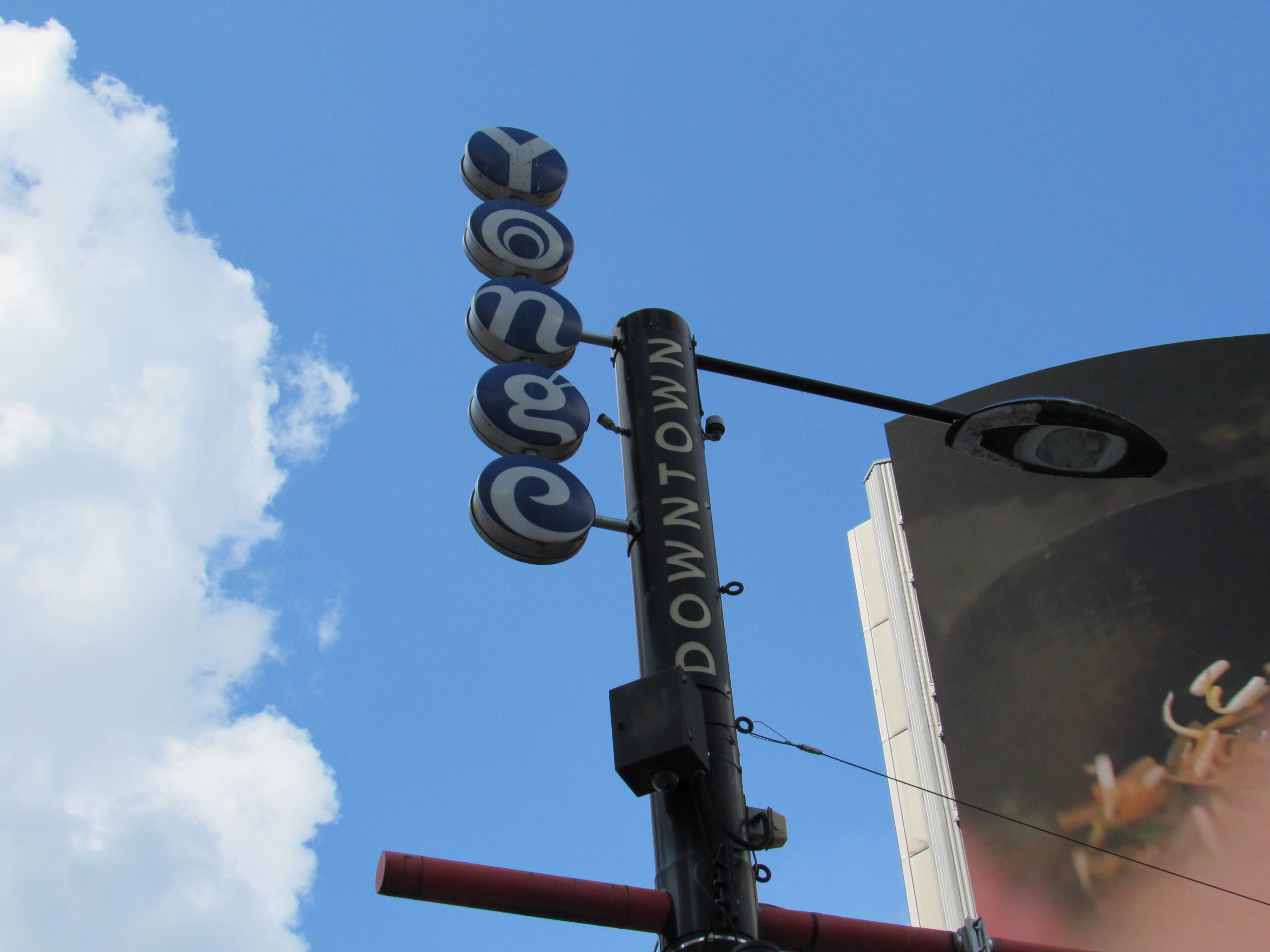 A vertical sign that reads "Downtown Yonge" in vertical letters set in front of a blue sky with clouds.