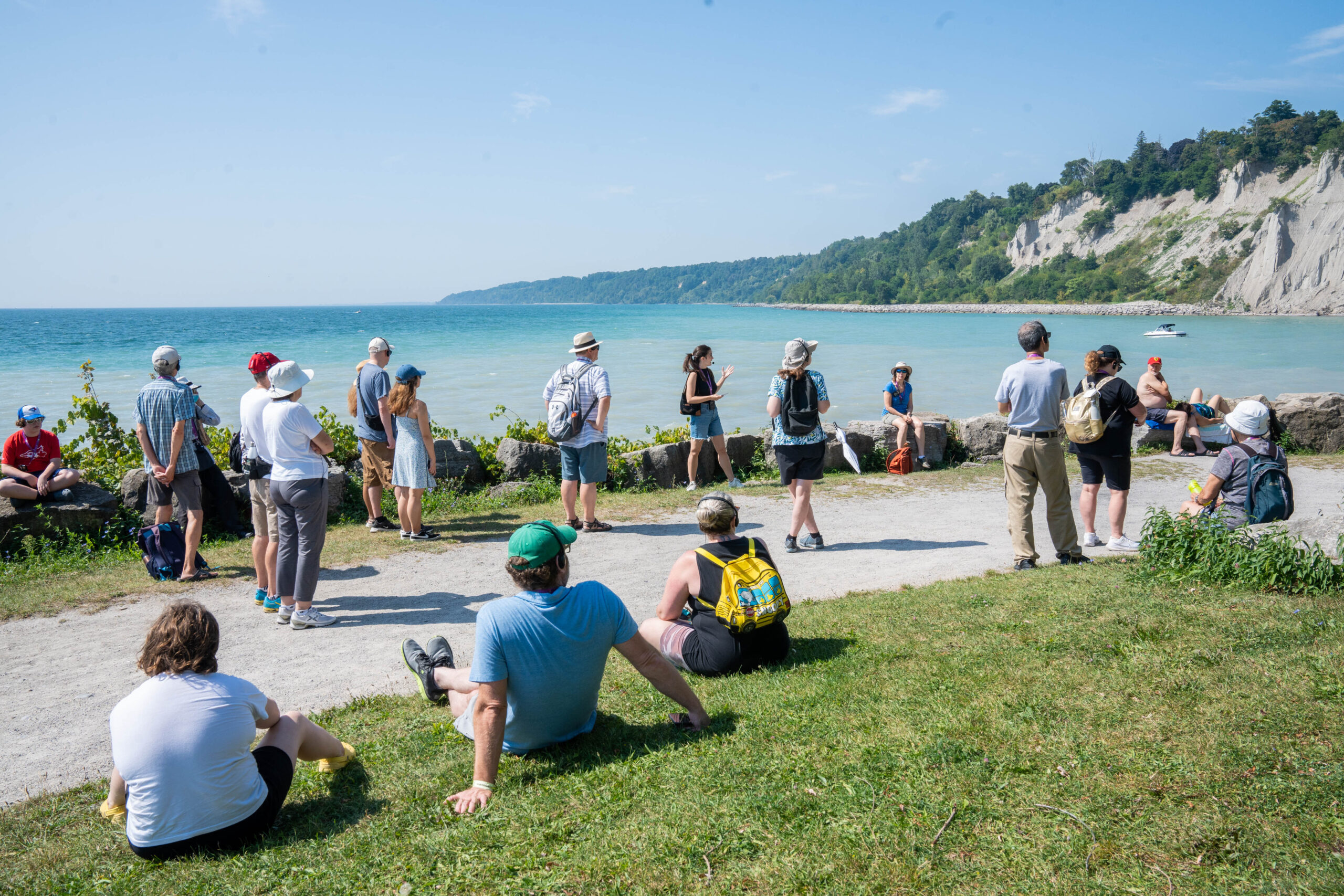 A large group of participants spread around the bluffs looking at the tour guide and looking out into the water.