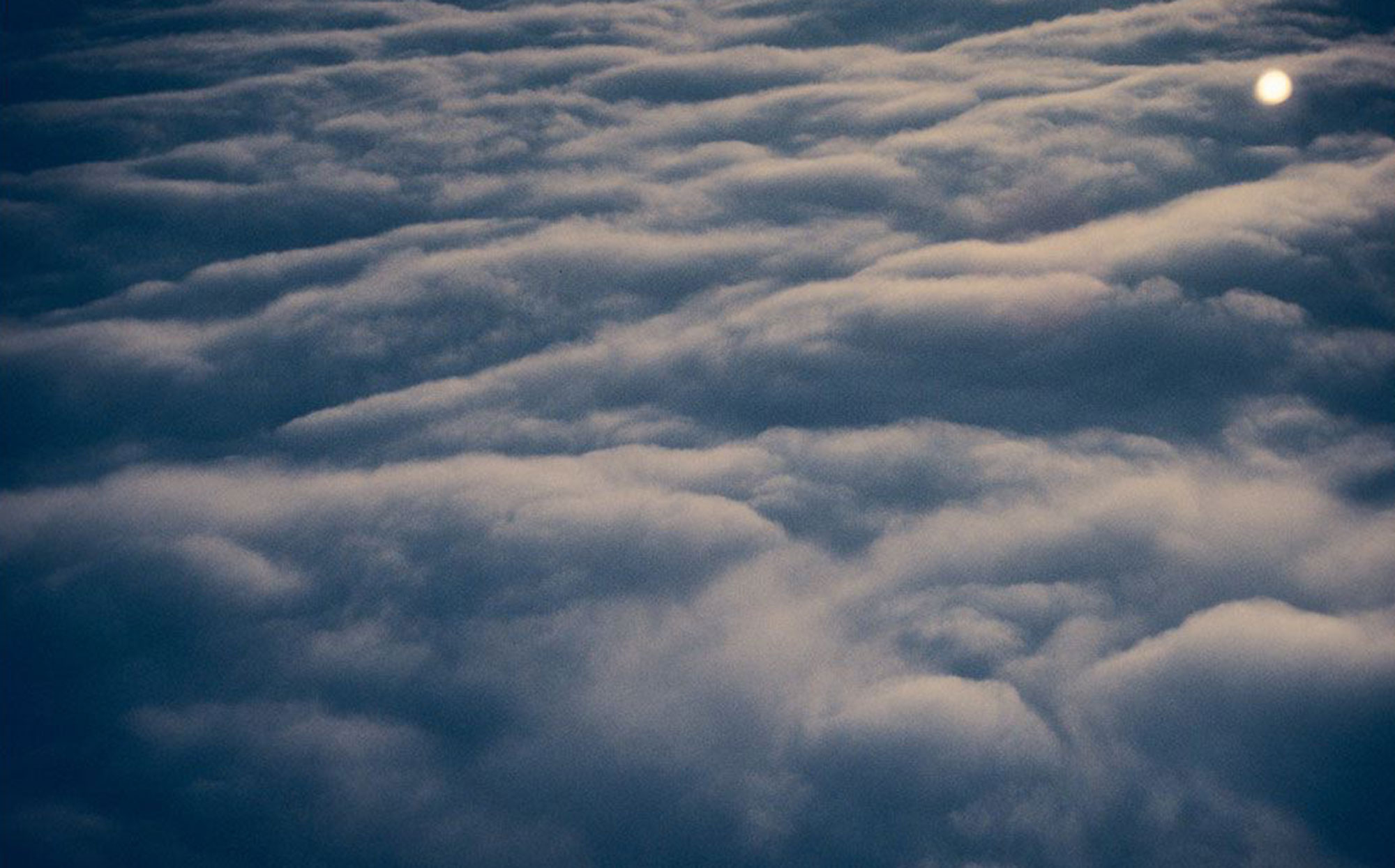 Colour photograph of a layer of clouds taken from above, most likely from the window of an airplane at sunrise or sunset.