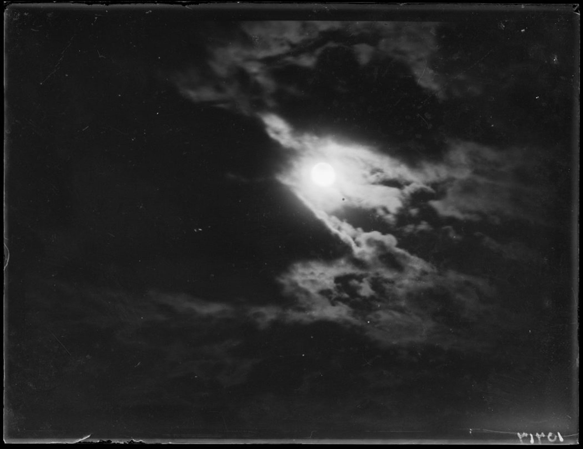 Black and white photo of a full moon partially obscured by clouds taken at night
