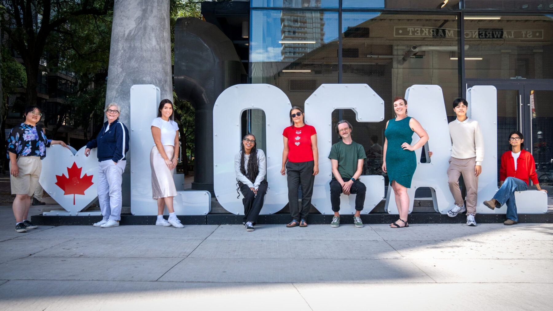 Photo of nine people posing with a sign that has a heart shape with maple leaf and the letters LOCAL.