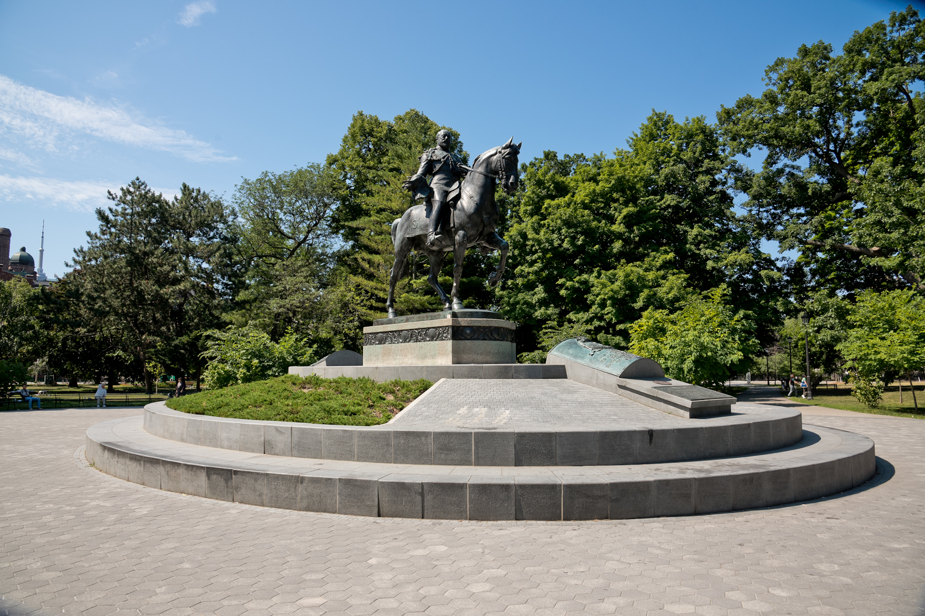 Image of a monument of a man on a horse raised on a plinth in a landscaped park setting.