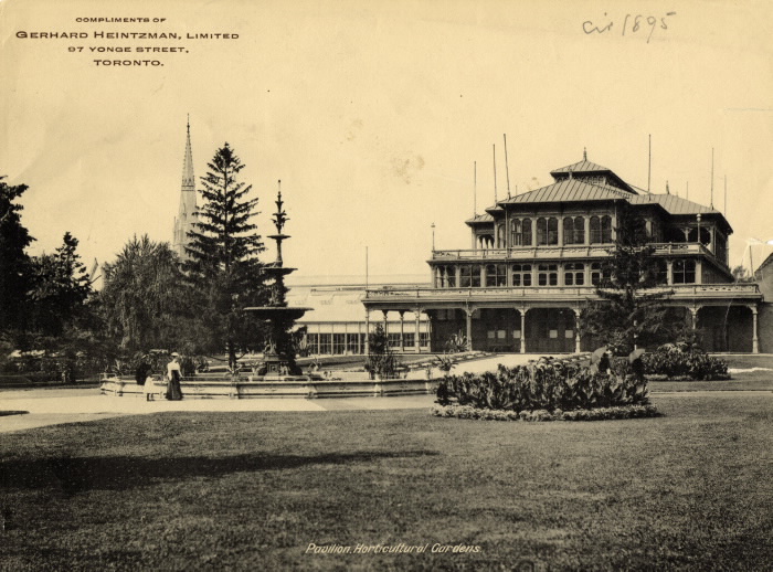 Sepia-toned photo of a multi-roofed building with a large sculptural fountain, pine trees, and large garden grounds.