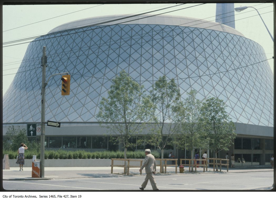 Modern building dominates image. Building comprises a large curved roof made of interconnected glass panels.