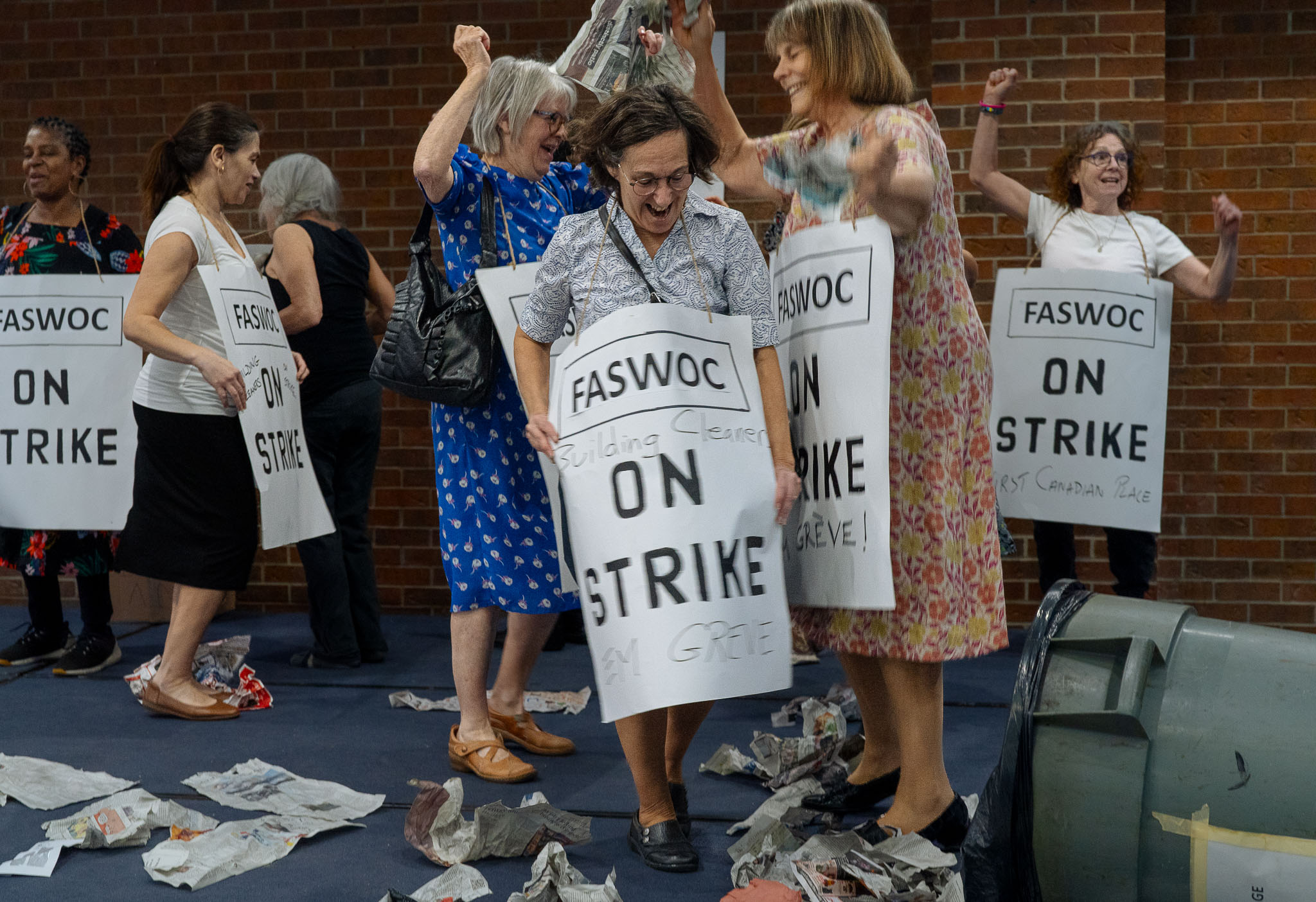 A group of actors on stage holding strike signs with their fist in the air. The signs read "FASWOC building cleaner ON STRIKE"