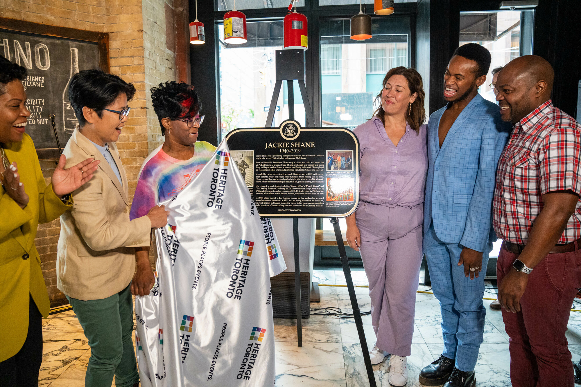Image of six people smiling after unveiling a plaque commemorating the singer Jackie Shane.
