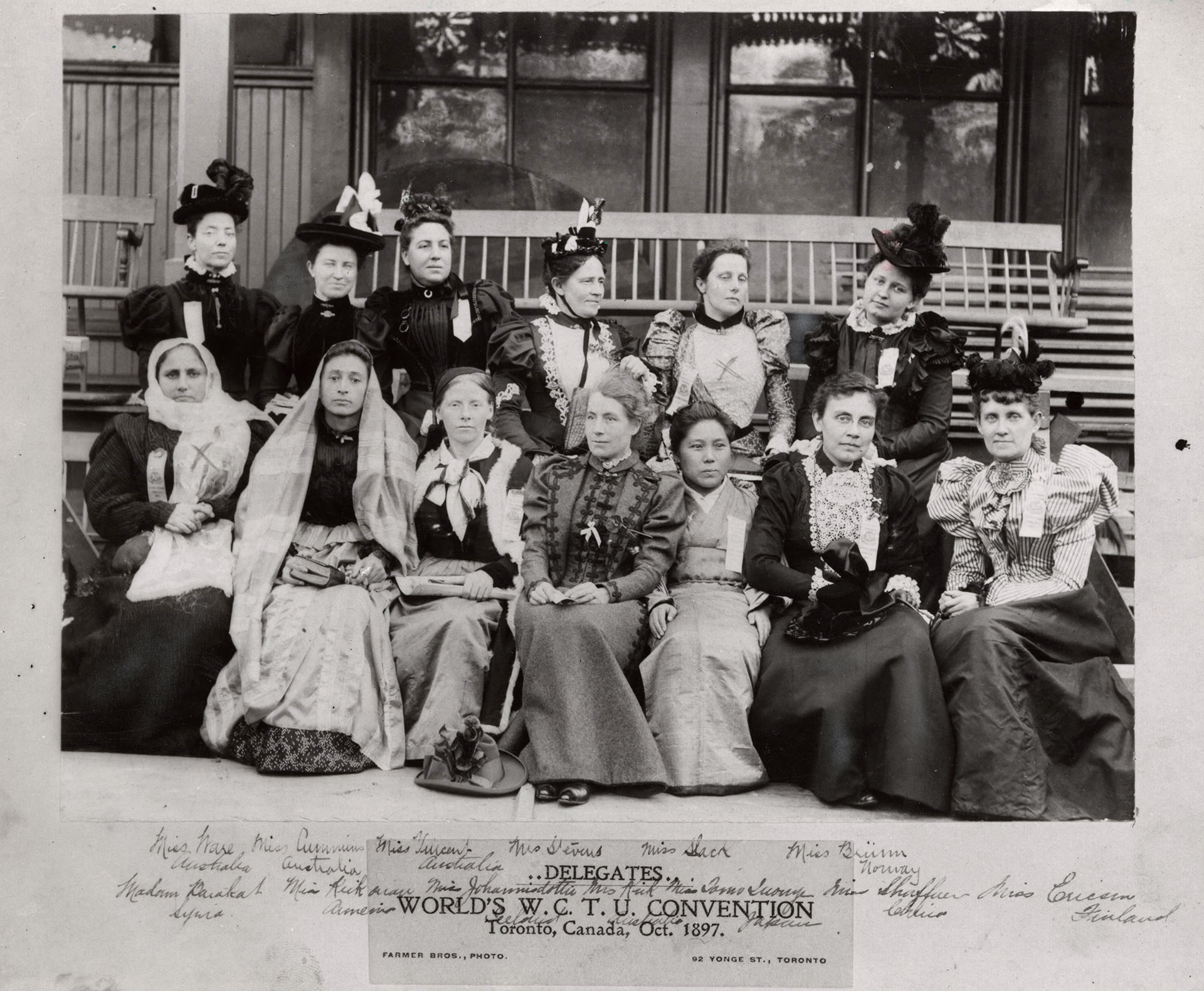 Black and white photo of a group of women in long dresses of all kinds sitting on the steps of a building. The text at the bottom of the photo reads, "..Delegates.. World's W. C. T. U. Convention Toronto, Canada, Oct. 1897. Farmer Bros., Photo 92 Yonge Street". The names of the women are scribbled in pencil over top of the caption and across the bottom of the image.
